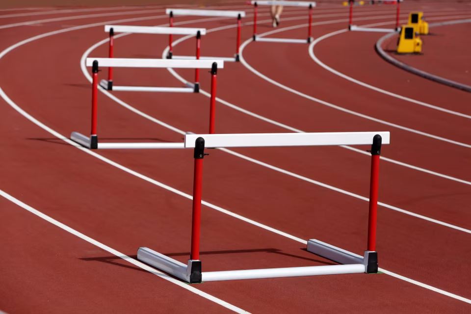 Mehrere rote und weiße Hürden stehen auf einer roten Laufbahn mit weißen Linien