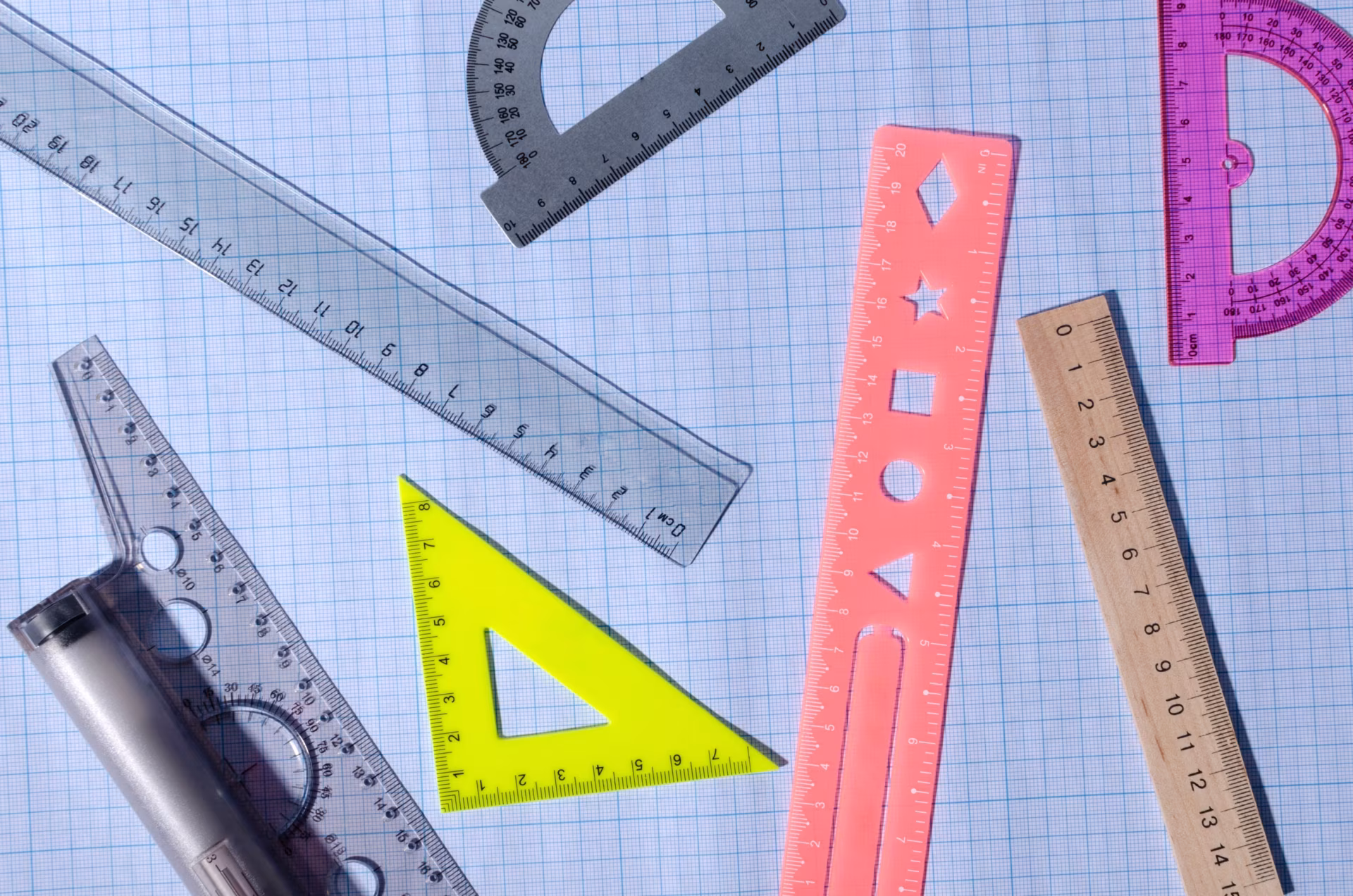 Mehrere Lineale und Geodreiecke in verschiedenen Farben liegen auf kariertem Papier.