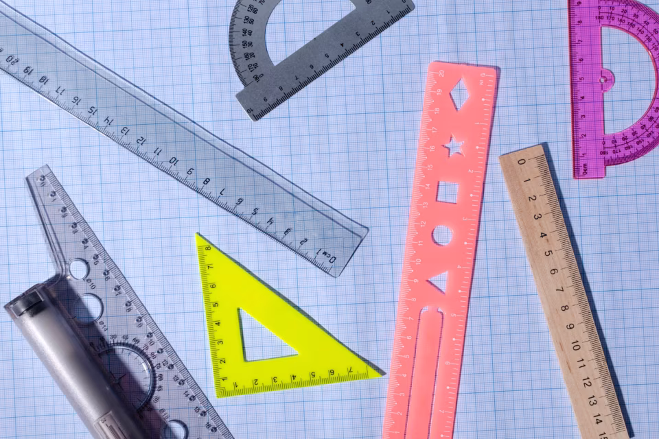 Mehrere Lineale und Geodreiecke in verschiedenen Farben liegen auf kariertem Papier.