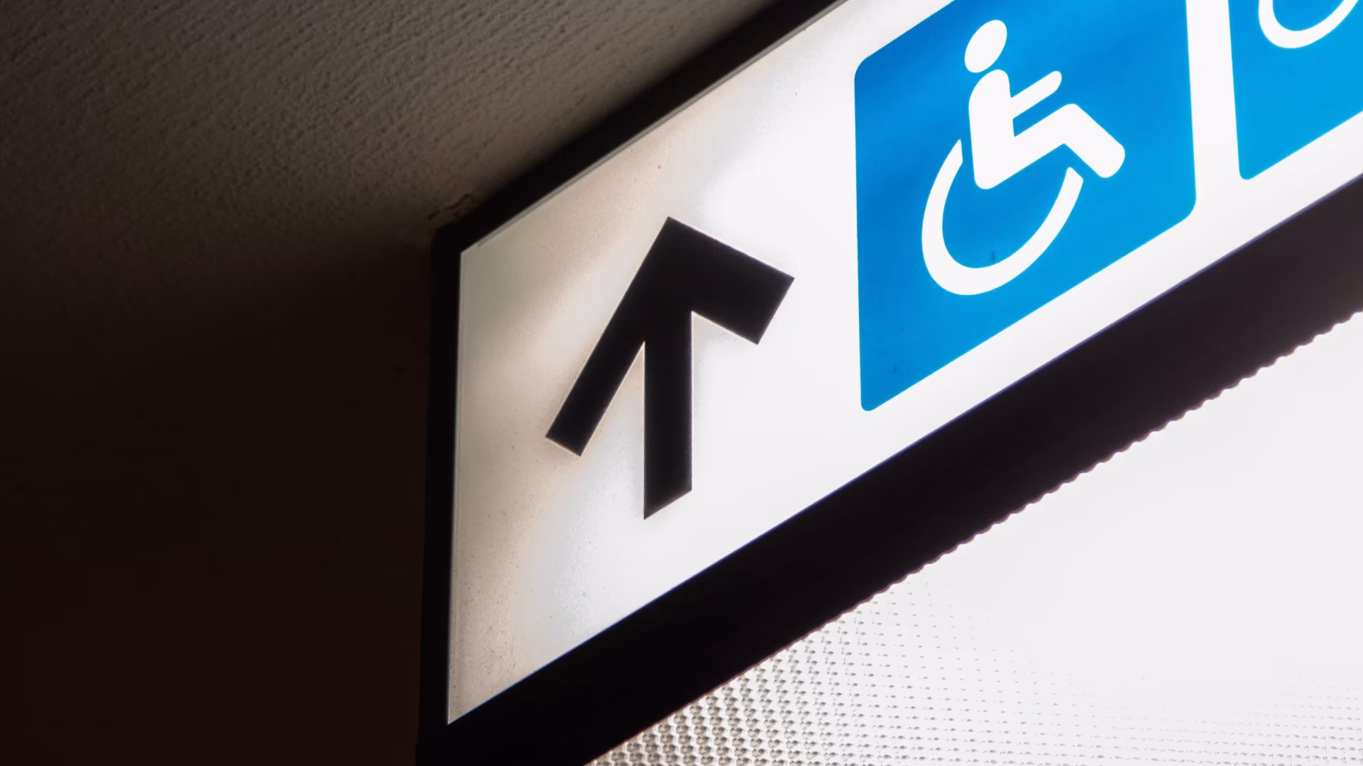 Wegweiser mit Pfeil nach oben und Rollstuhl-Symbol auf blauem Grund