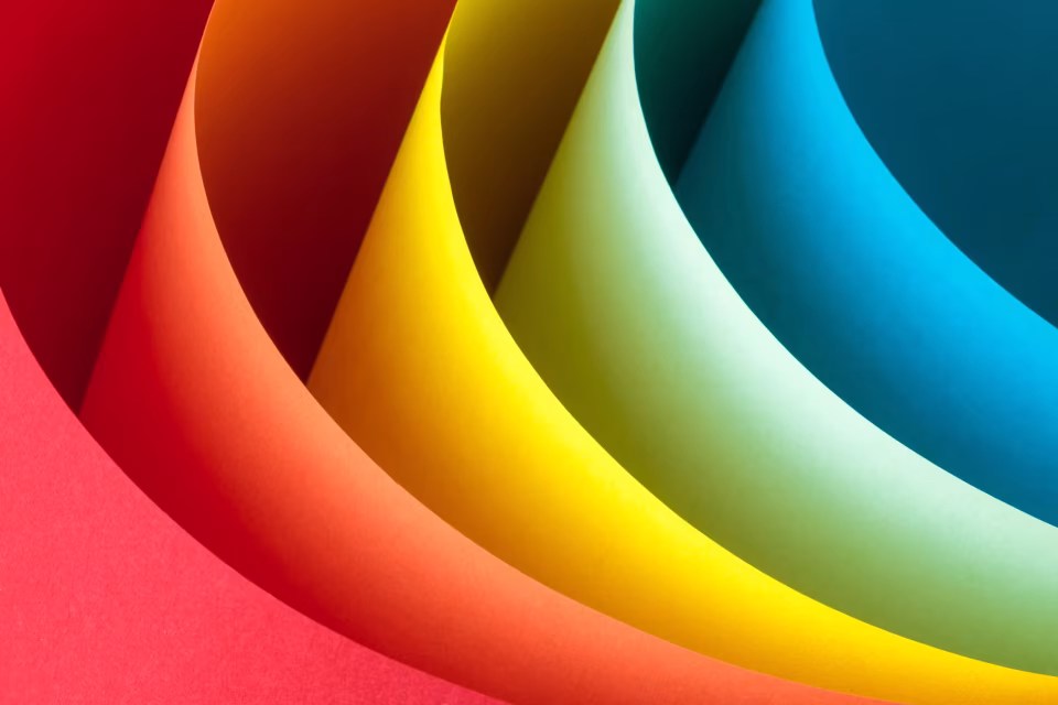 Gebogene Papierbögen in Rot, Orange, Gelb, Hellgrün und Blau, übereinandergelegt und von oben fotografiert