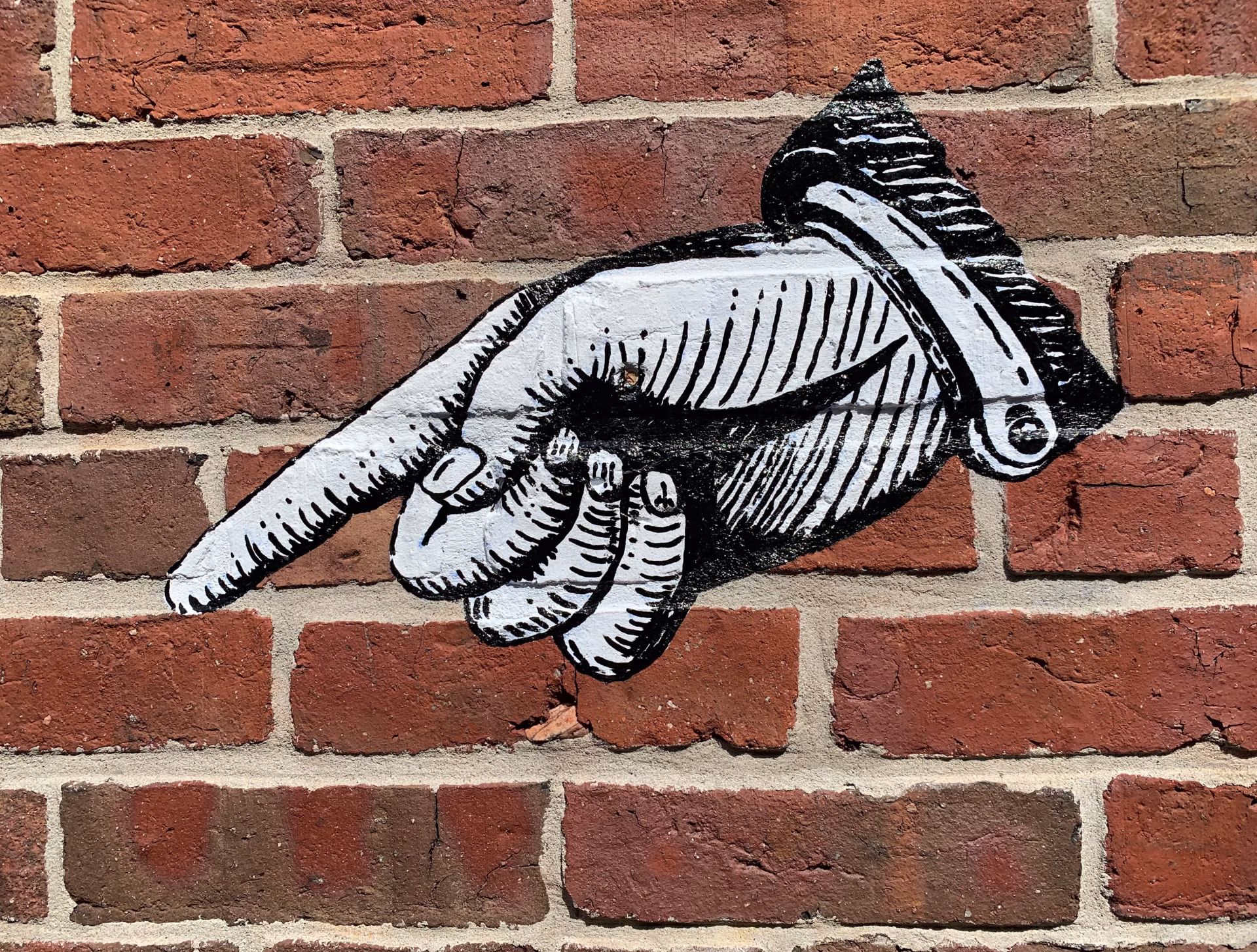Große schwarz-weiße Wandmalerei einer zeigenden Hand auf roter Backsteinwand