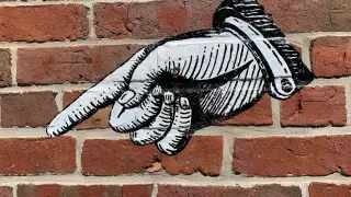 Straßenkunst auf einer Backsteinwand mit einem Finger, der auf etwas zeigt