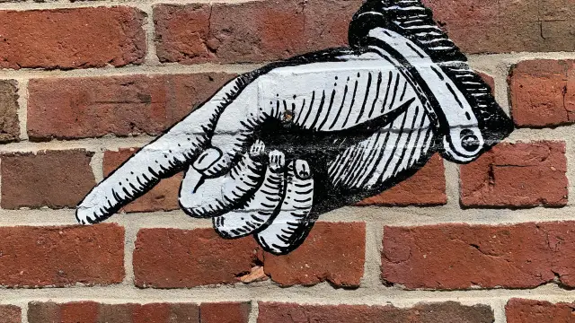 Straßenkunst auf einer Backsteinwand mit einem Finger, der auf etwas zeigt
