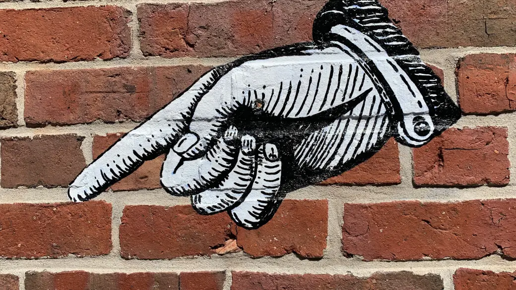 Straßenkunst auf einer Backsteinwand mit einem Finger, der auf etwas zeigt